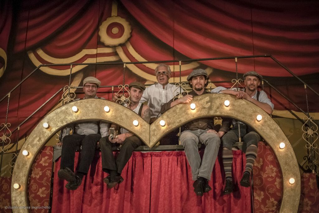 Cinque uomini con coppola seduti sull'arco a forma di cuore di lampadine
