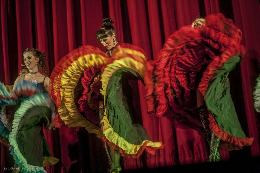 Tre ballerine roteano gonne rosso giallo verde davanti al sipario