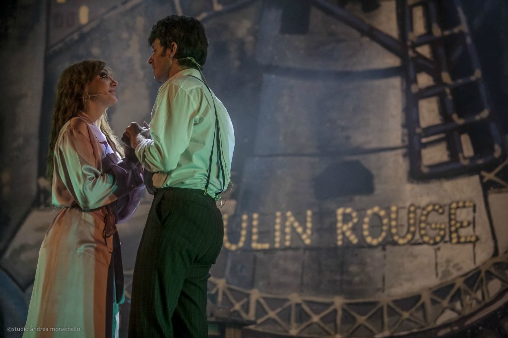 Coppia di amanti si stringe le mani davanti all'insegna luminosa Moulin Rouge