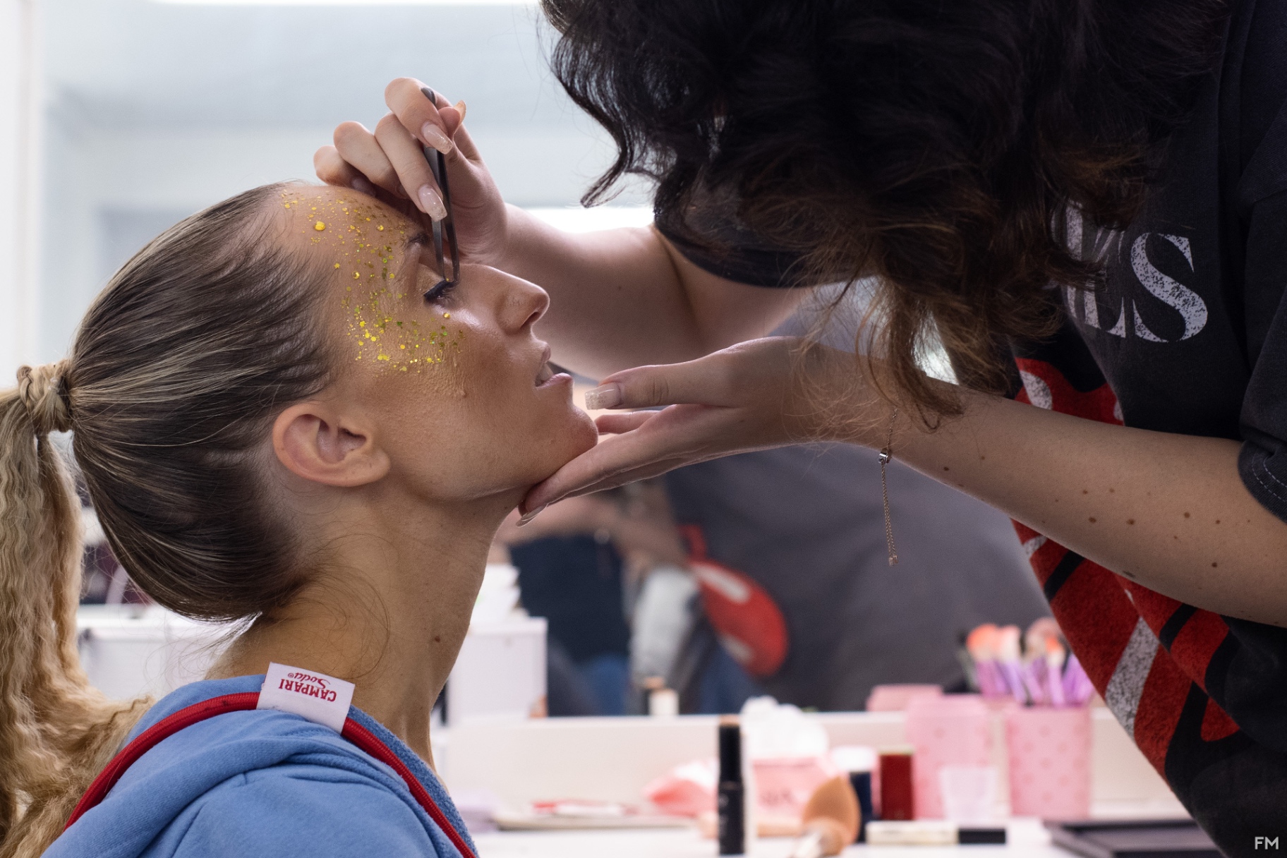 Profilo di attrice con glitter dorato sulla tempia mentre le viene disegnato l'eyeliner