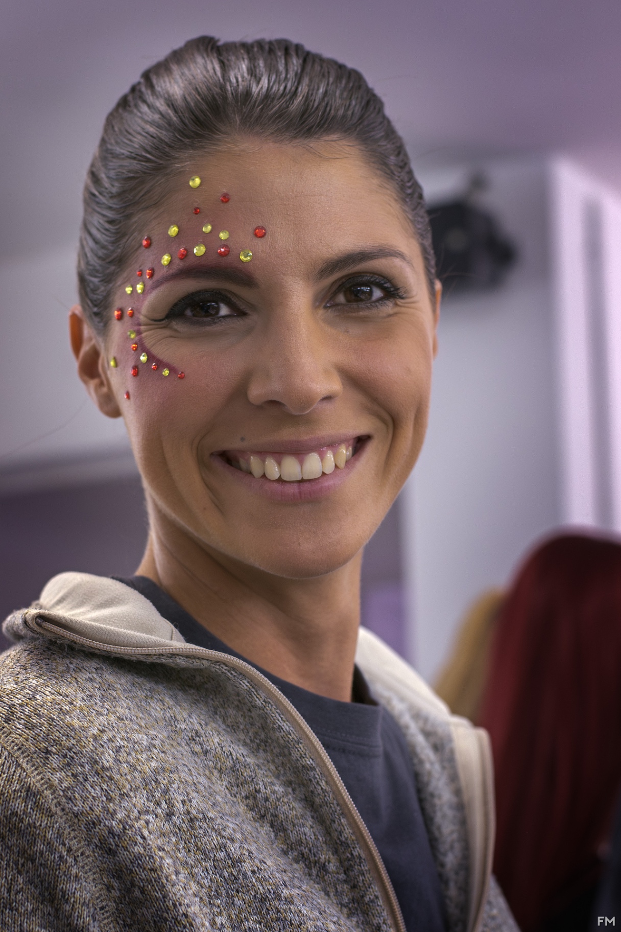 Ritratto sorridente di attrice con strass rossi e gialli applicati intorno all'occhio