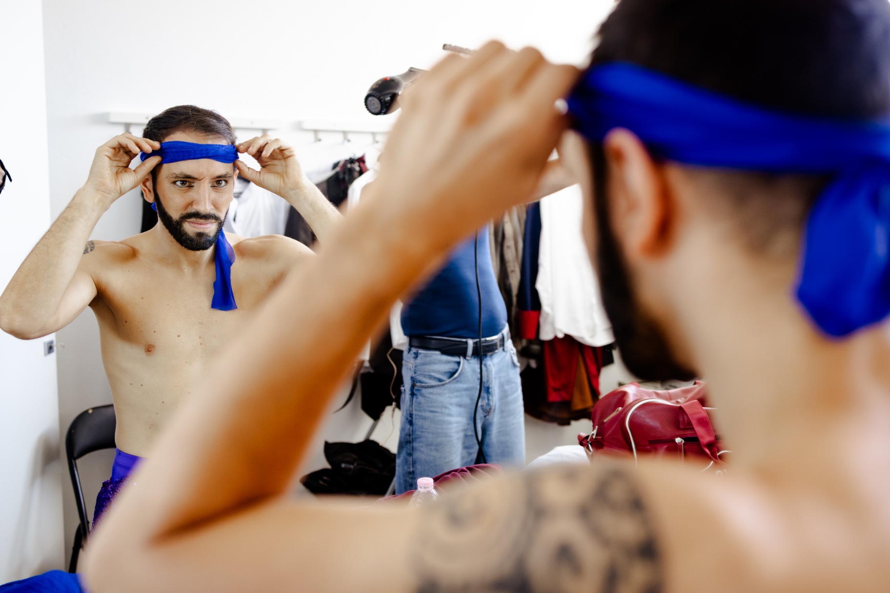 Attore a torso nudo si annoda una bandana blu davanti allo specchio del camerino