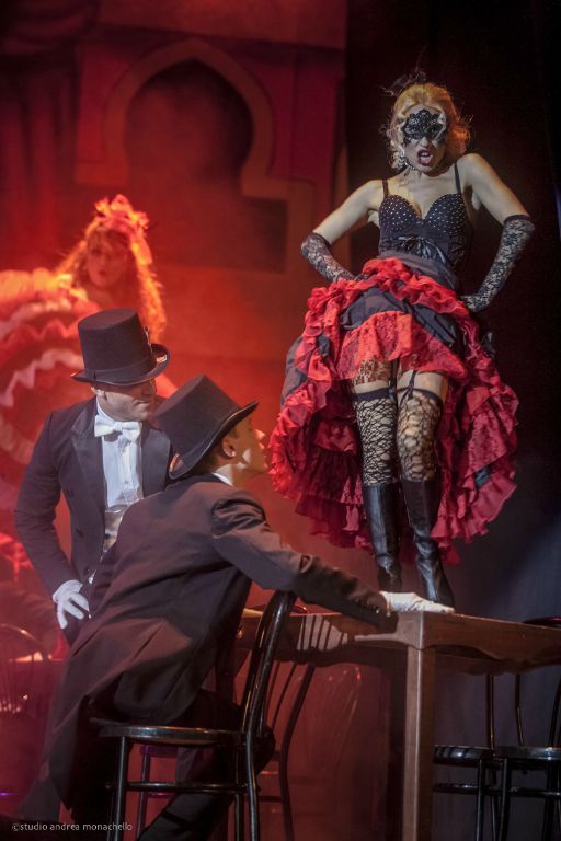 Ballerina mascherata in corsetto e gonna rossa in piedi sul tavolo davanti a due clienti