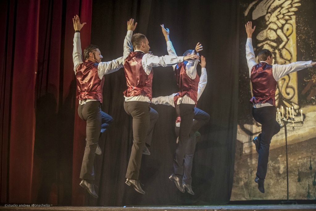 Quattro ballerini in gilet bordeaux saltano sincronizzati a braccia alzate