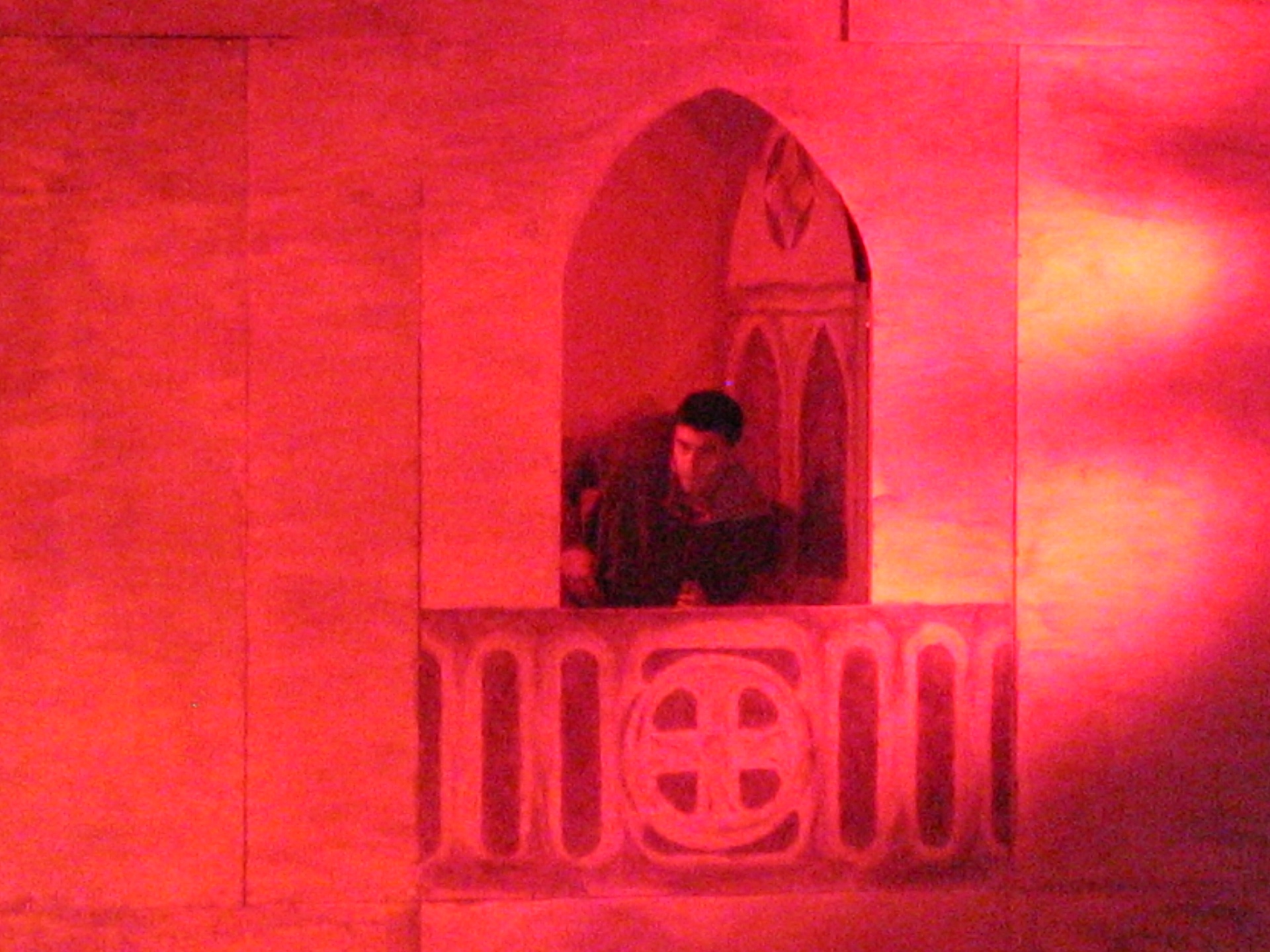 Uomo affacciato a una bifora gotica illuminata di rosso