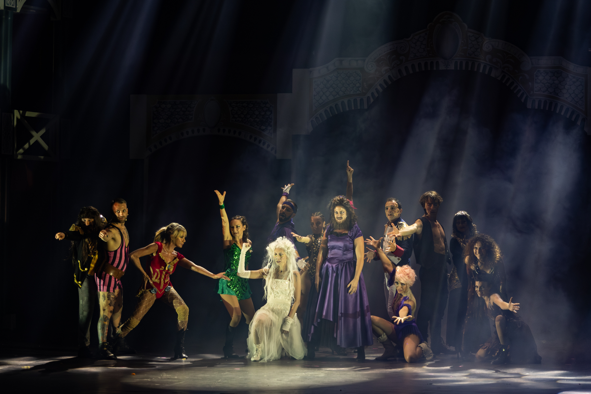 Cast dei freaks raccolto attorno alla donna in bianco inginocchiata al centro del palco