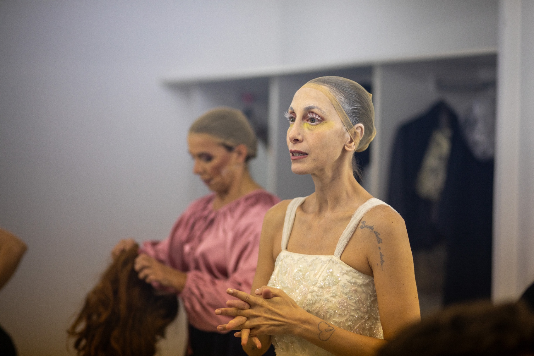 Due ballerine con calotta e trucco chiaro in camerino, una in primo piano di profilo con abito ricamato