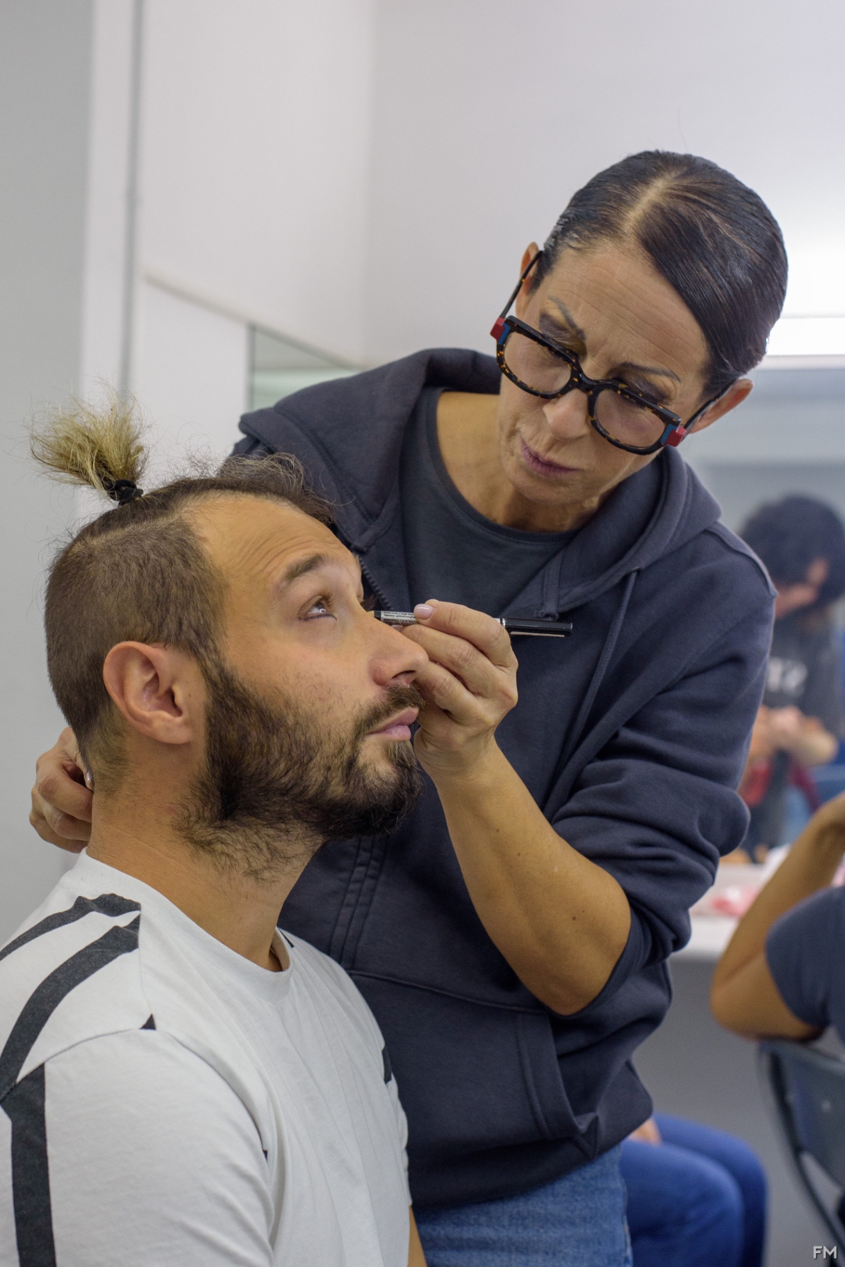 Truccatrice con occhiali applica il trucco al volto di un attore seduto