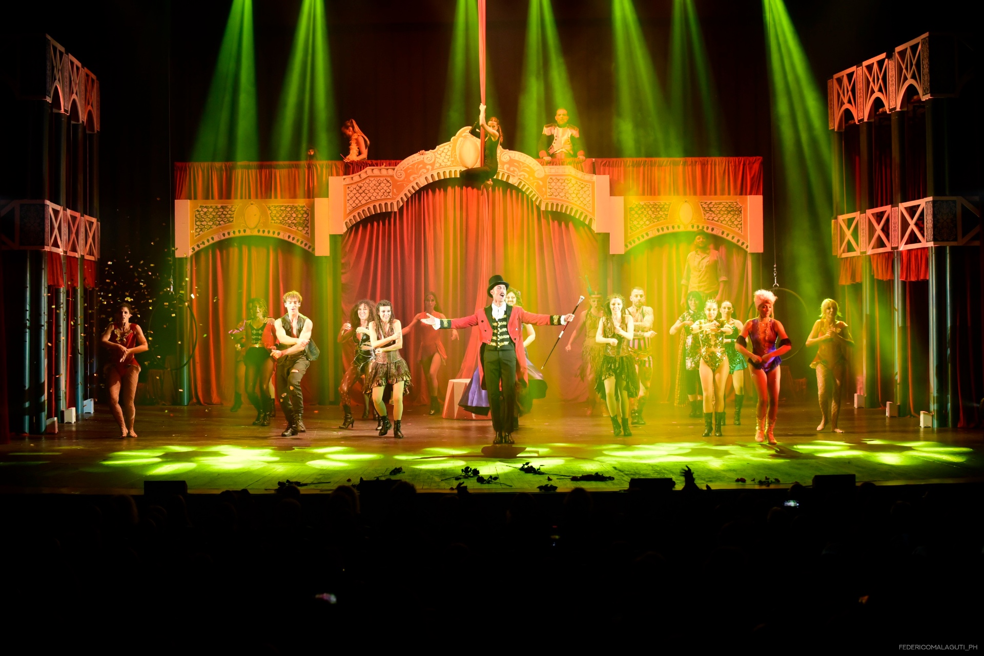 Finale con showman in rosso al centro sotto luci verdi e sipario rosso illuminato