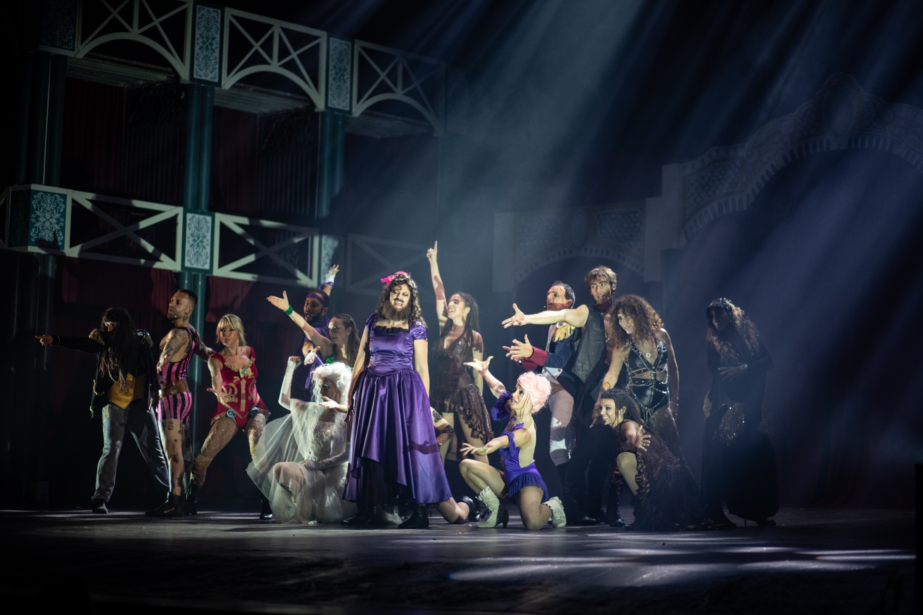 Cast al completo con la donna barbuta in abito viola al centro sotto raggi di luce