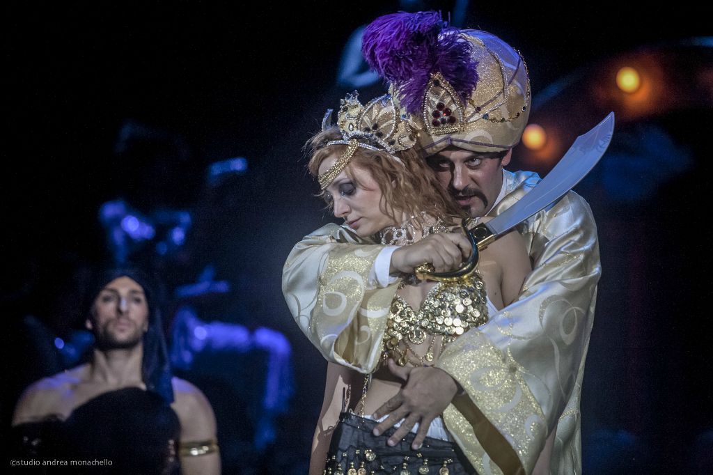 Maharajah con turbante e piume viola tiene la scimitarra al collo di una donna con corona