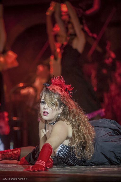 Donna sdraiata a terra con guanti e piume rosse in scena dai toni rossi
