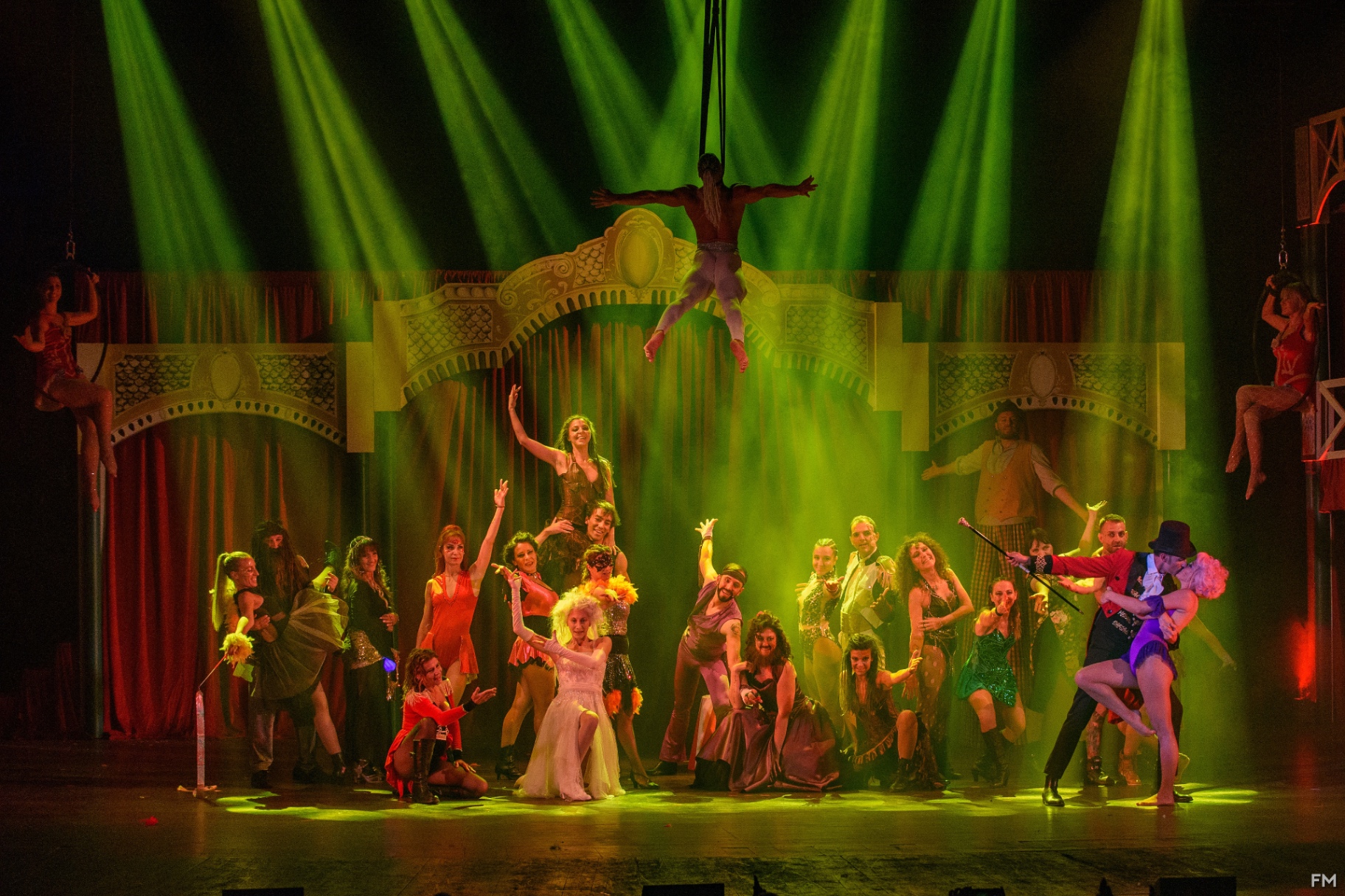 Grande tableau del cast con acrobata sospesa a croce sopra l'ensemble