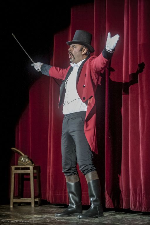 Maestro di cerimonie in marsina rossa, cilindro e bastone urla davanti al sipario