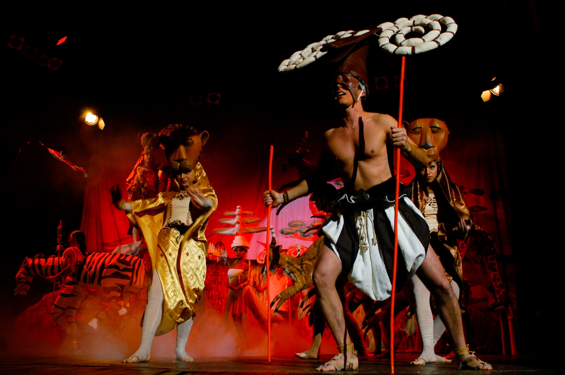 Danza di gruppo con maschere di leone e copricapo di piume sotto luci rosse