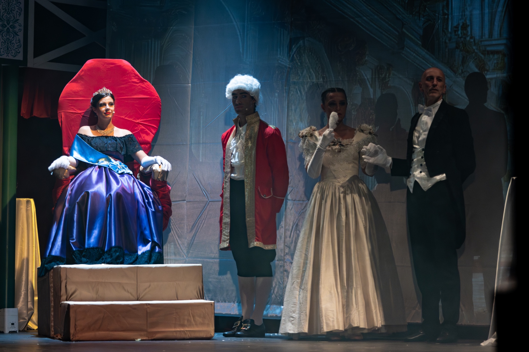 Regina in abito blu sul trono rosso accanto a paggio, dama e gentiluomo in frac