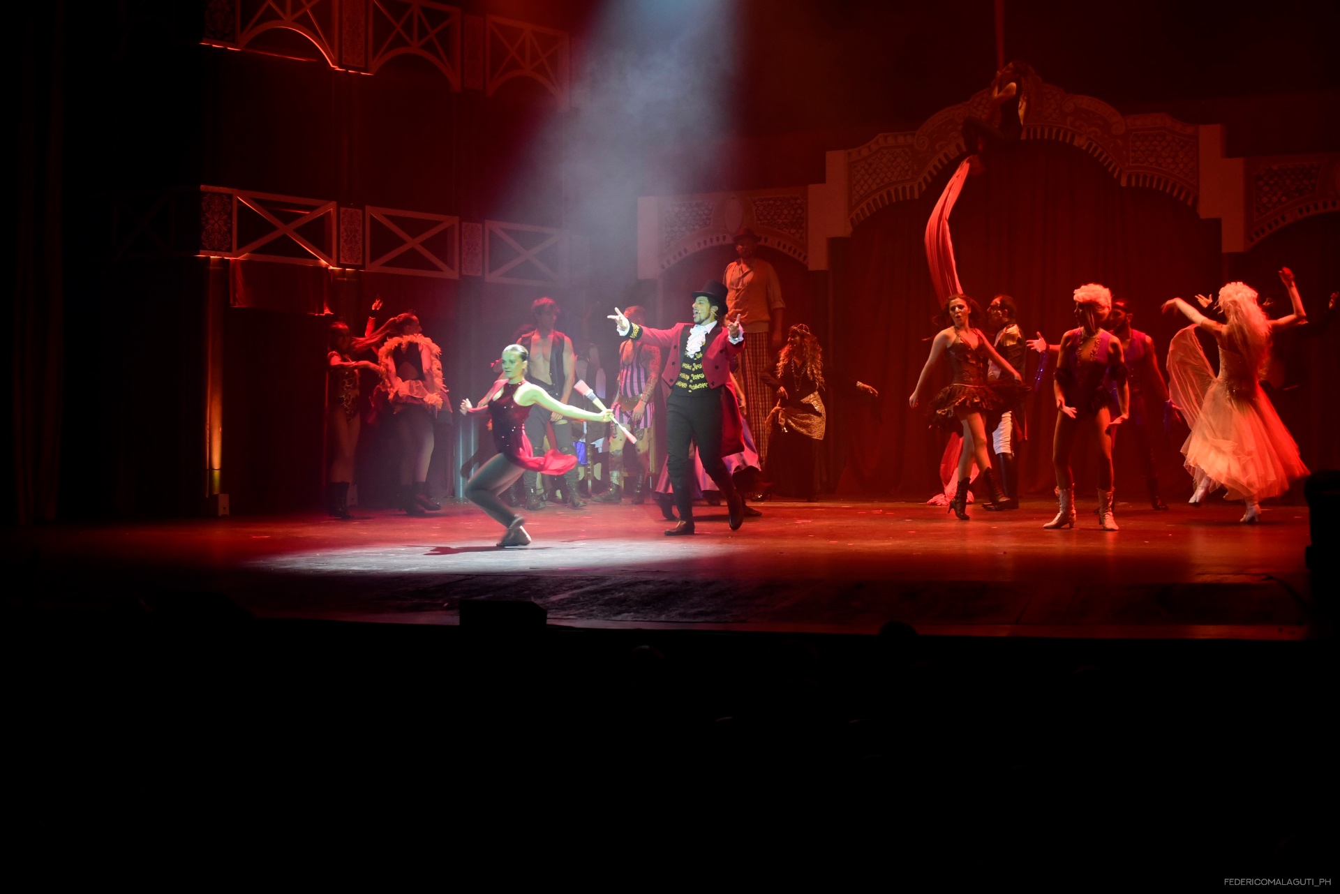 Coppia di ballerini in primo piano su palco illuminato di rosso, compagnia sullo sfondo