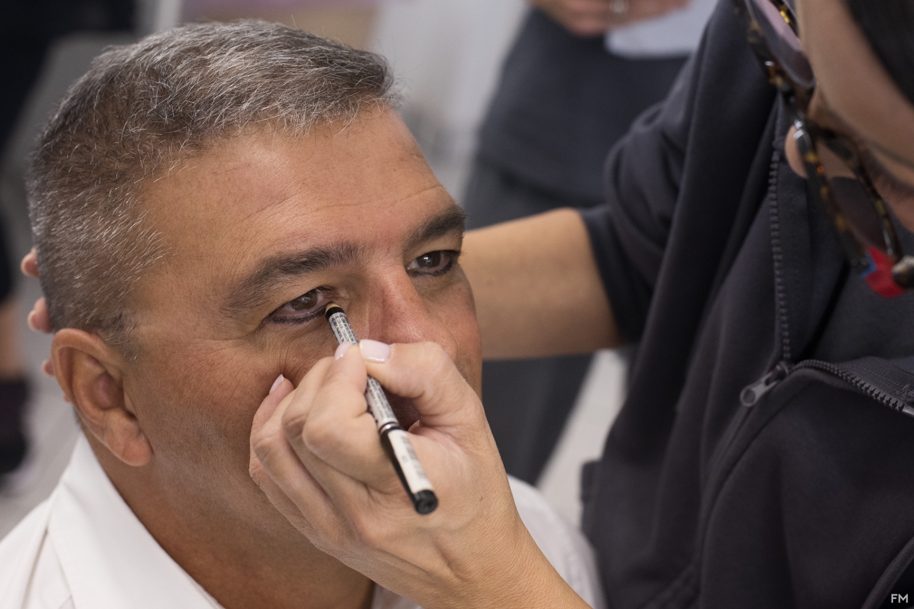 Primo piano di uomo con capelli brizzolati mentre gli viene applicato l'eyeliner nero