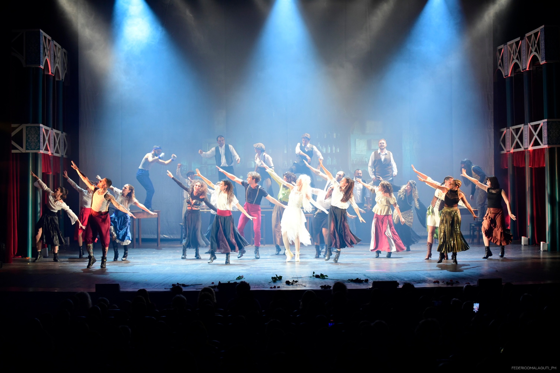 Compagnia in coreografia dinamica con braccia aperte sotto luci bianche e blu