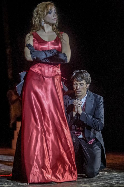 Donna in abito rosso e uomo inginocchiato che la implora
