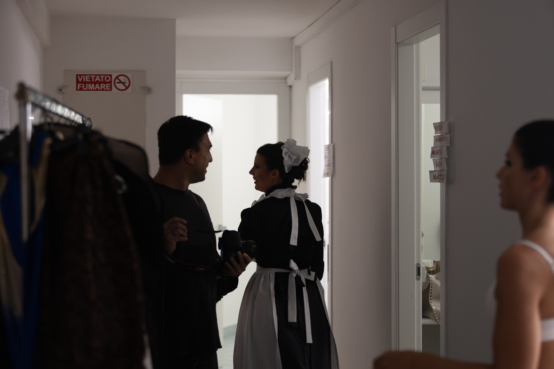 Fotografo di scena conversa con attrice in costume da cameriera in corridoio dei camerini