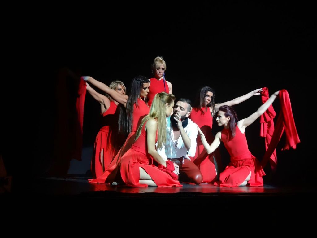 Cerchio di danzatrici in rosso attorno a un uomo in bianco