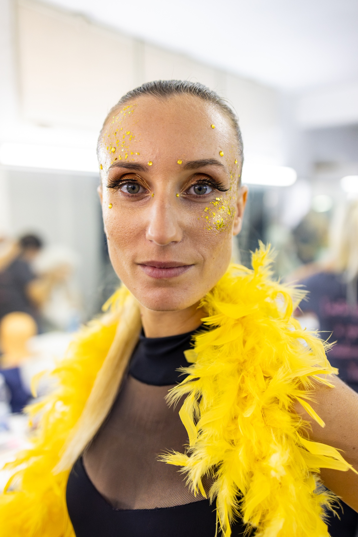 Ritratto di ballerina con capelli raccolti, glitter giallo intorno agli occhi e boa di piume gialle sulle spalle