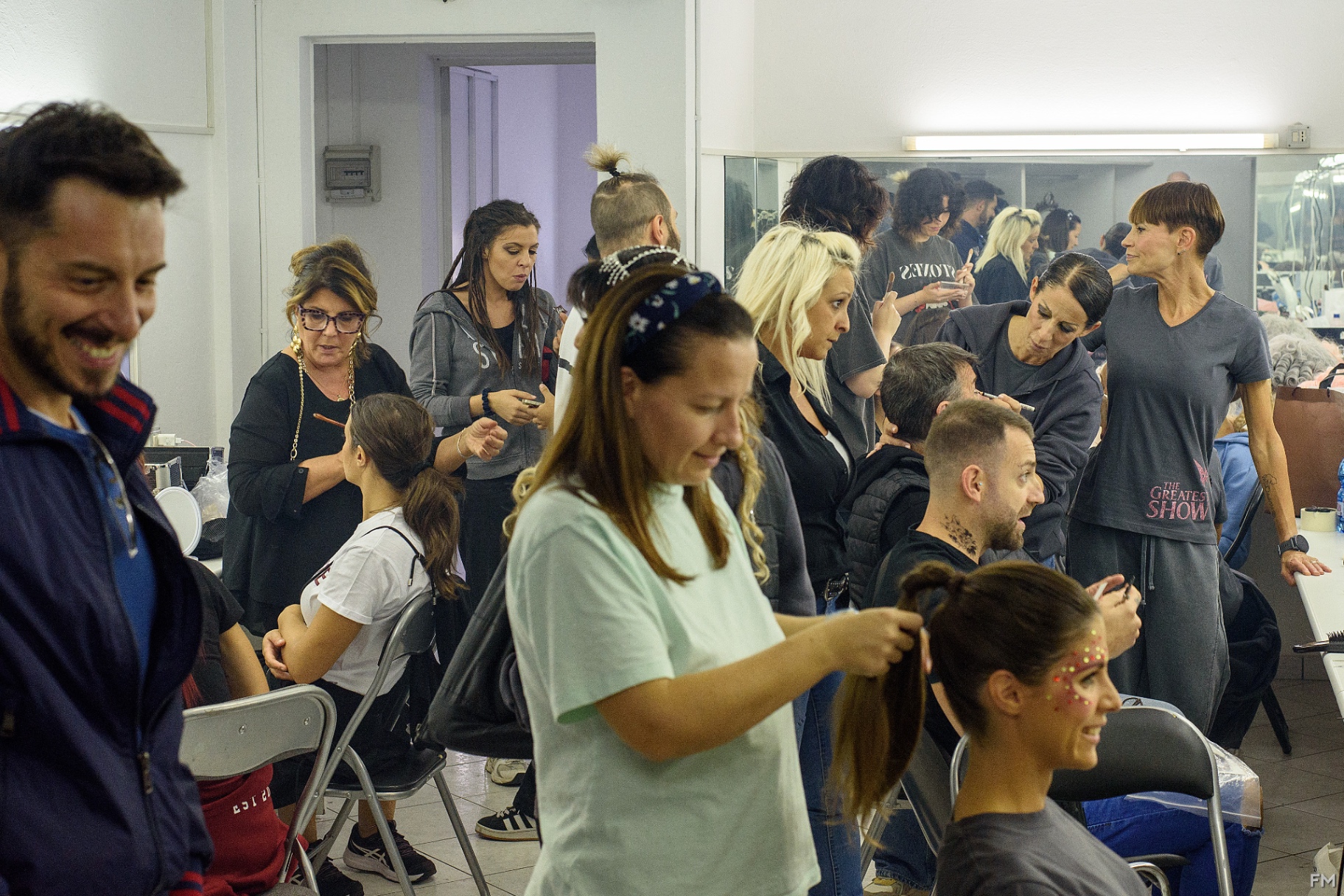 Camerino affollato con truccatrici al lavoro e cast in preparazione davanti agli specchi