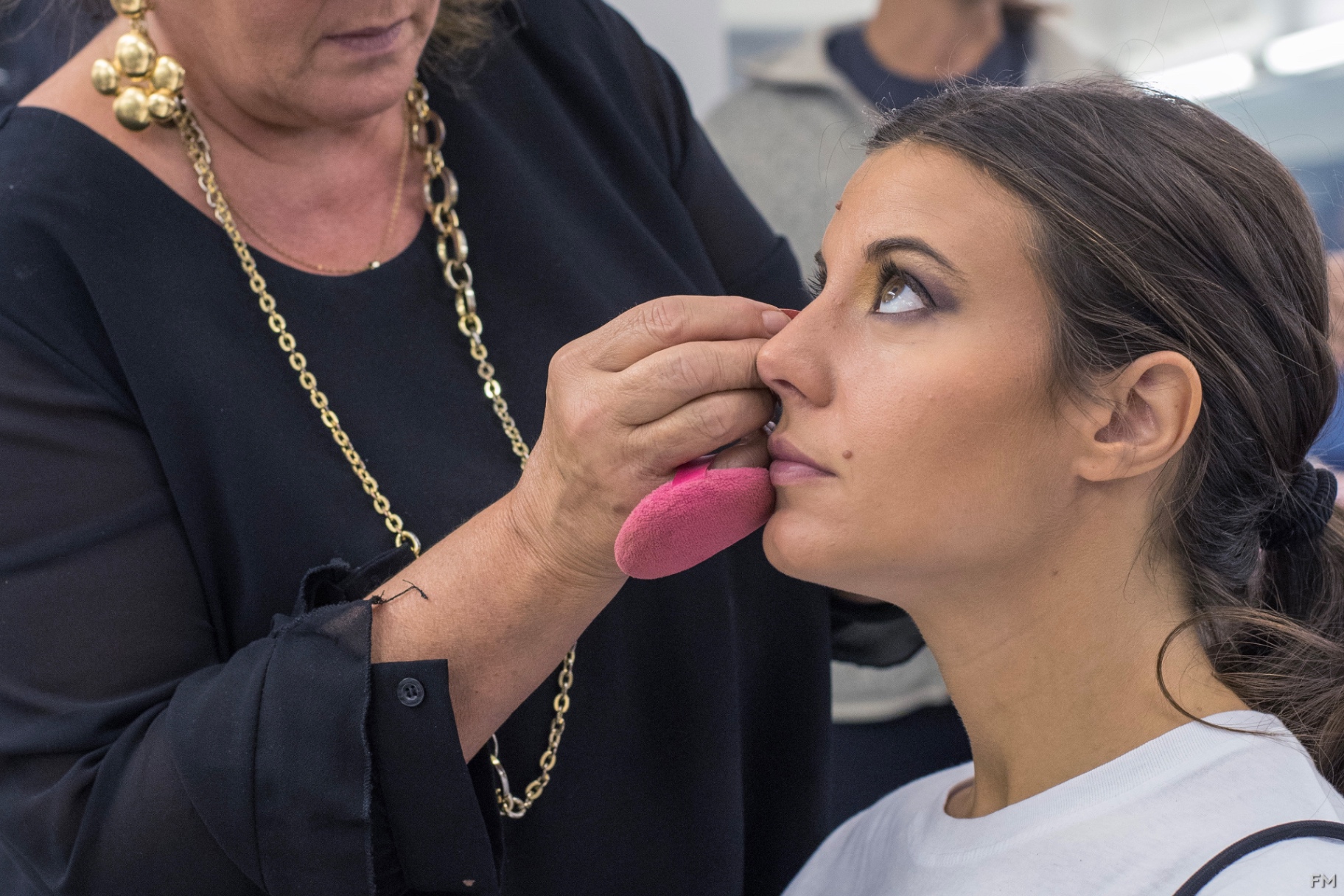 Truccatrice in nero applica fondotinta con spugna rosa al viso di una giovane