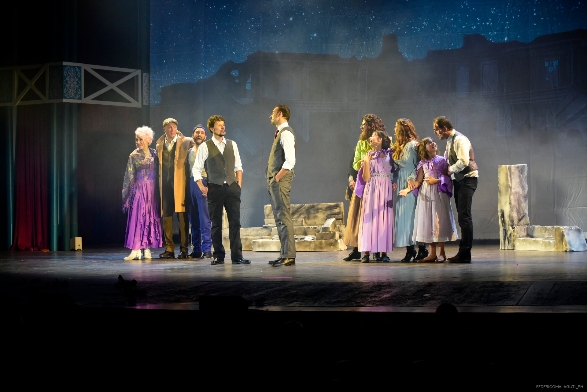 Gruppo di attori in costume su sfondo di città in rovina sotto cielo stellato