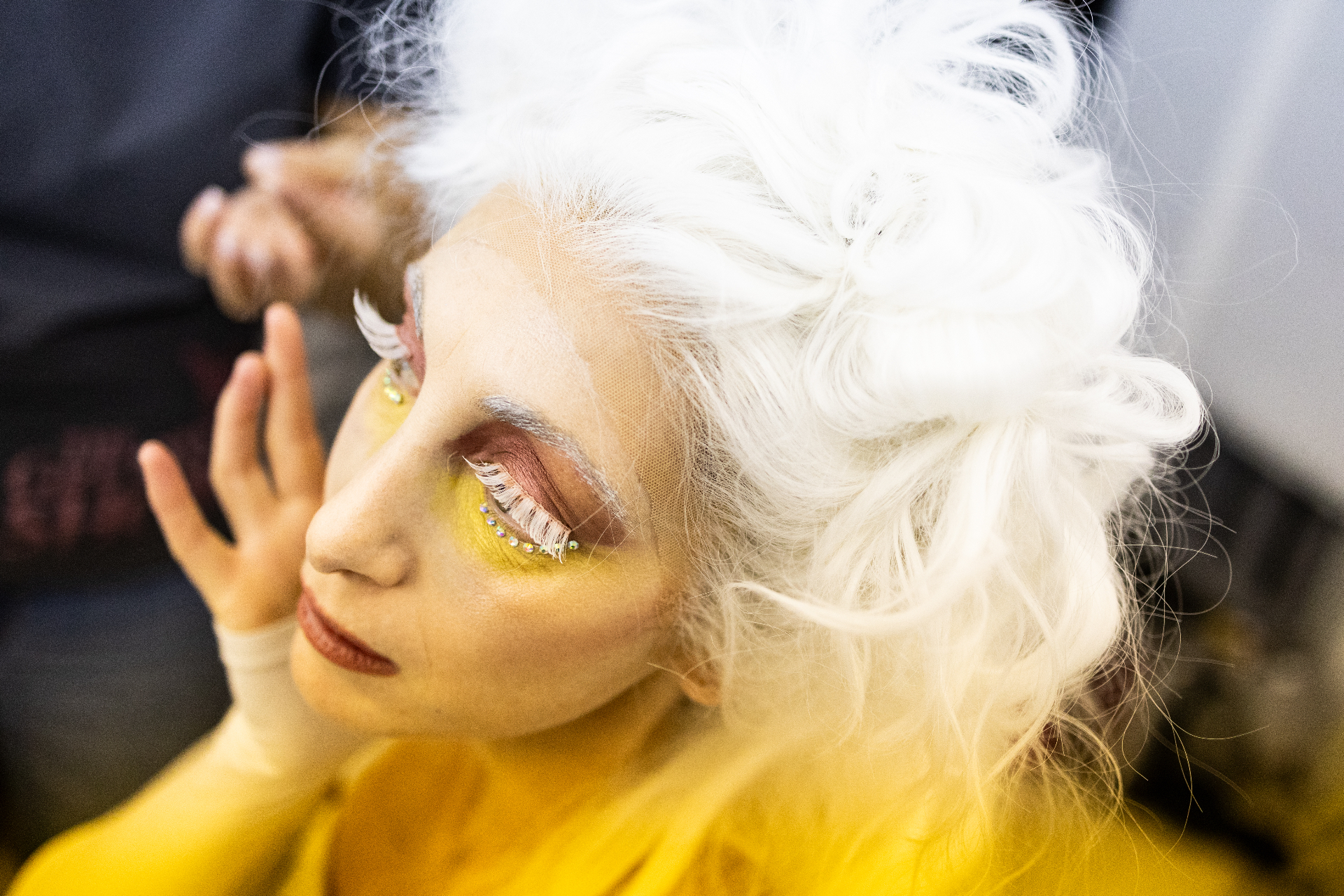 Primo piano di ballerina con parrucca bianca voluminosa, ciglia bianche e trucco giallo con strass
